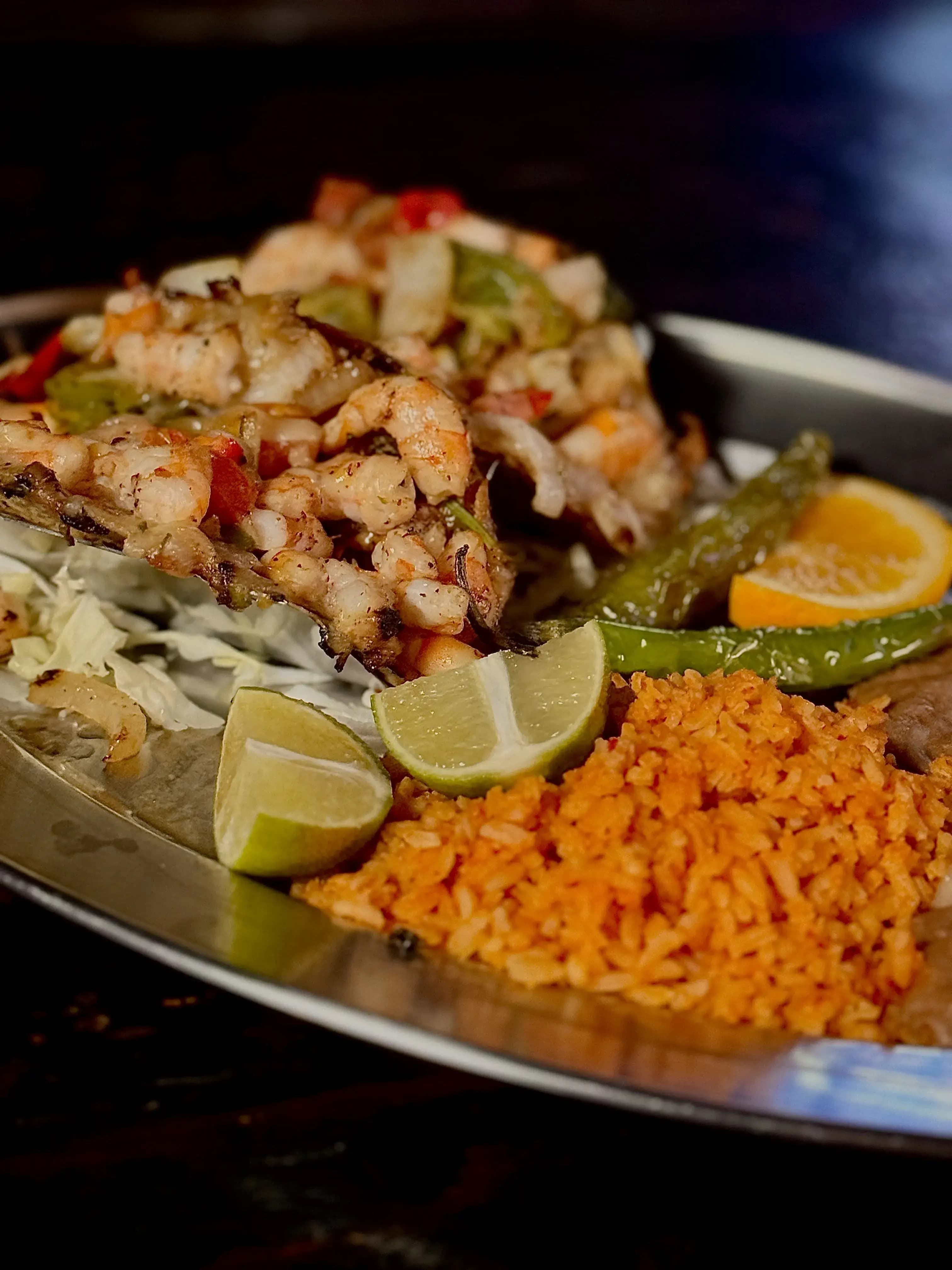 2 shrimp-filled tacos held up by a silver stand and sitting on a plate alongside beans and rice.